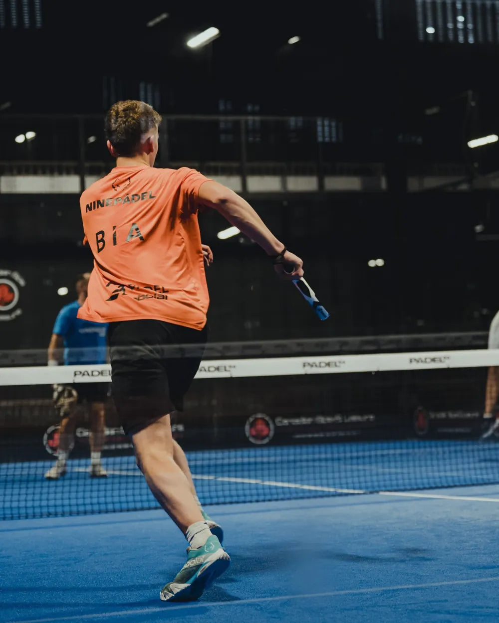 NINEPADEL player in an orange shirt on court at Padel54